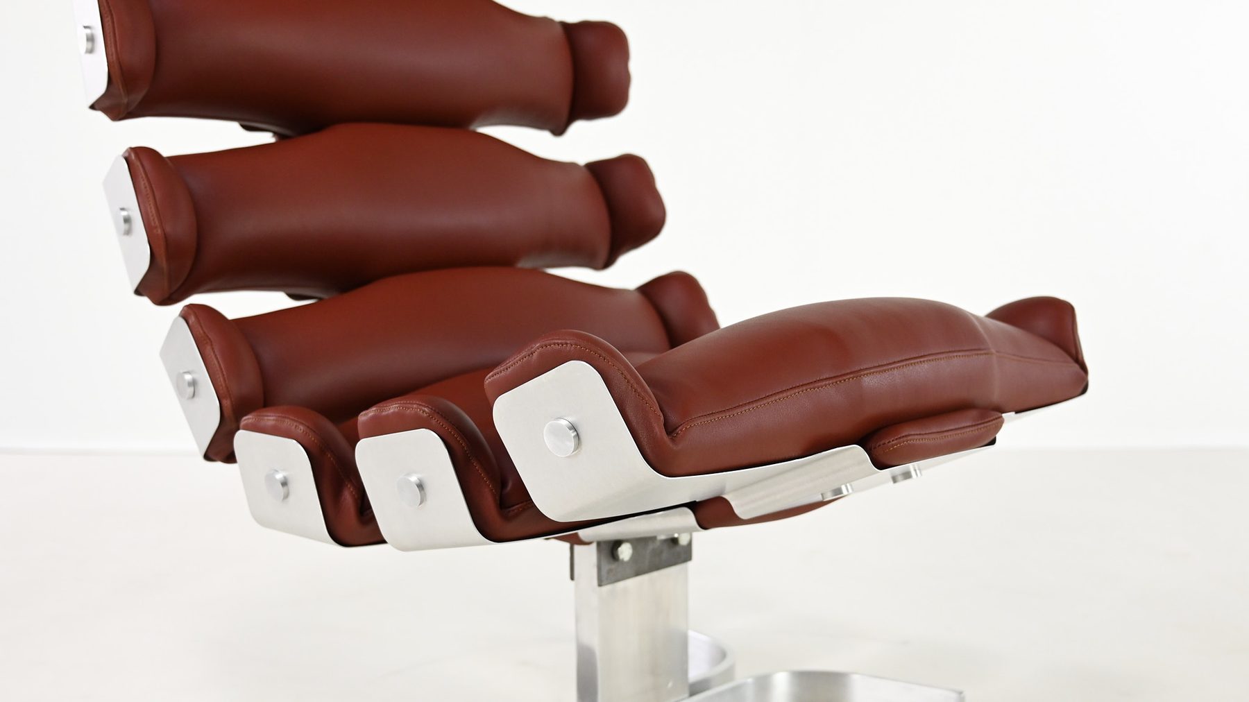 Un fauteuil de cuir brun dont le dossier est fait de segments arrondis, sur un pied d'aluminium
