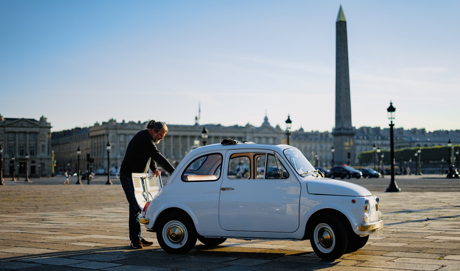 Un homme ouvre la portière d'une Fiat 500 blanche, place de la Concorde à Paris, devant l'obélisque