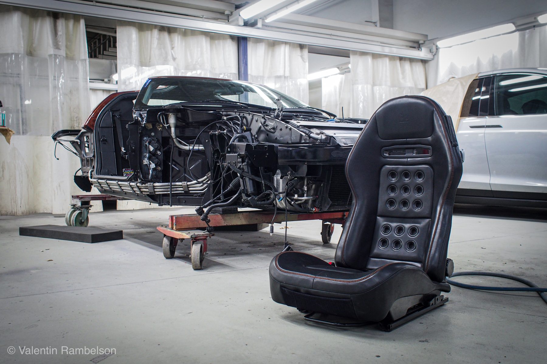 Un siège baquet noir posé à côté de la caisse d'une voiture dont la carrosserie est déposée, dans un atelier