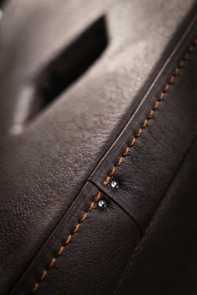 Couture sellier au fil orange sur un cuir brun, deux rivets chromés le long du bord