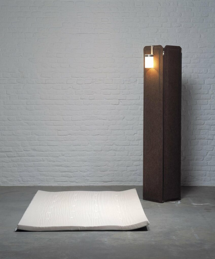 Jim de matali crasset : la colonne de feutre brun et sa lampe, avec le matelas posé au sol