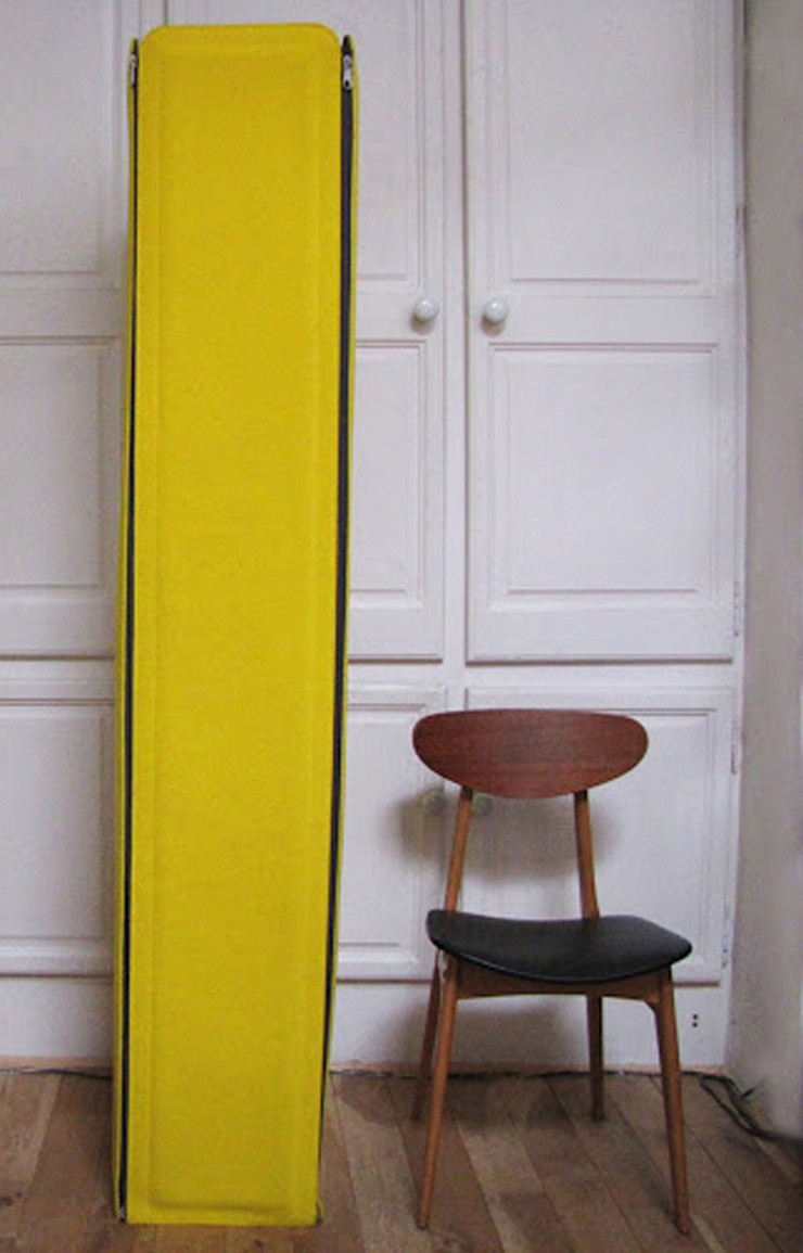 Jim plié : une colonne de feutre jaune dressée contre des portes blanches, à côté d'une chaise en bois